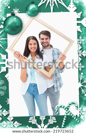 Happy young couple holding picture frame against christmas frame
