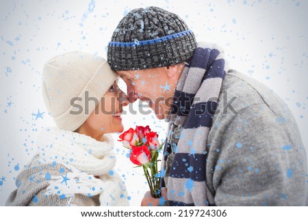 Happy mature couple in winter clothes with roses against snow falling