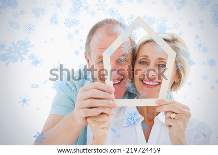Happy older couple holding house shape against snow falling