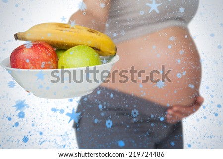 Pregnant woman showing fruit bowl to camera against snow falling
