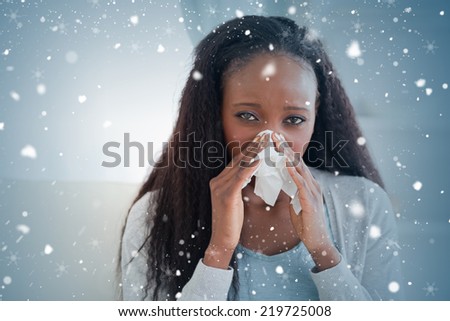 Composite image of close up of woman on sofa blowing her nose against snow falling