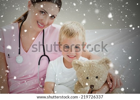Composite image of smiling little boy holding a teddy bear on a hospital bed against snow falling