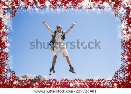 Handsome hiker jumping at the summit smiling at camera against snow