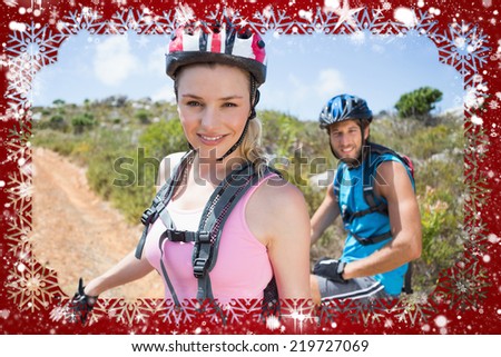 Fit couple cycling up mountain trail smiling at camera against snow