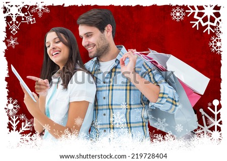 Happy couple with shopping bags and tablet against christmas themed snow flake frame