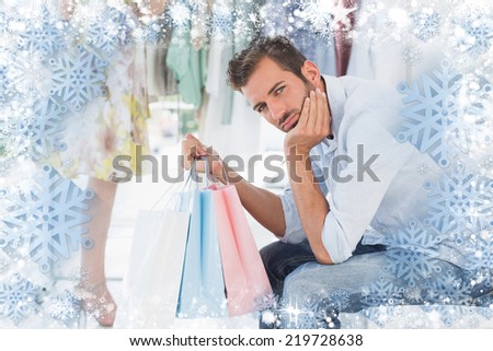 Bored man with shopping bags while woman by clothes rack against snow