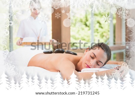 Beautiful woman receiving stone massage at health farm against fir tree forest and snowflakes