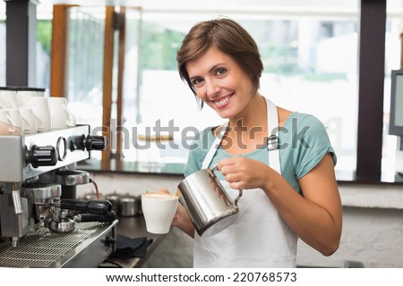 Pretty barista pouring milk into cup of coffee at the coffee shop