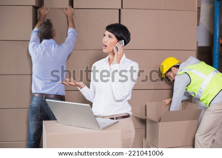 Warehouse manager using laptop and talking on phone in a large warehouse