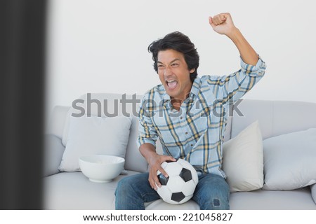 Portrait of a happy soccer fan cheering while watching tv