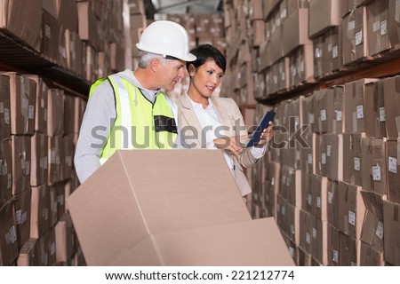 Warehouse worker moving boxes on trolley talking to manager in a large warehouse