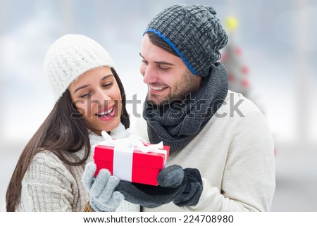 Winter couple holding gift against blurry christmas tree in room