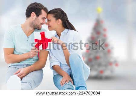 Young couple holding gift against blurry christmas tree in room