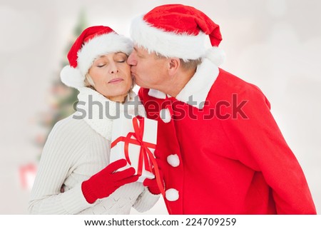 Festive mature couple holding gift against blurry christmas tree in room