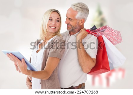 Happy couple with shopping bags and tablet pc against blurry christmas tree in room