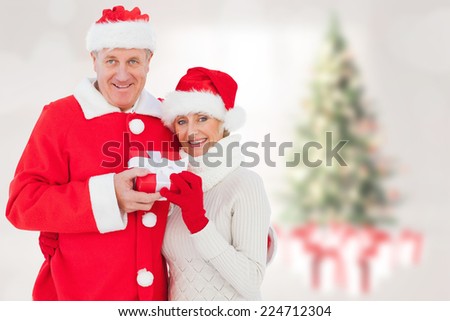 Festive mature couple holding gift against blurry christmas tree in room