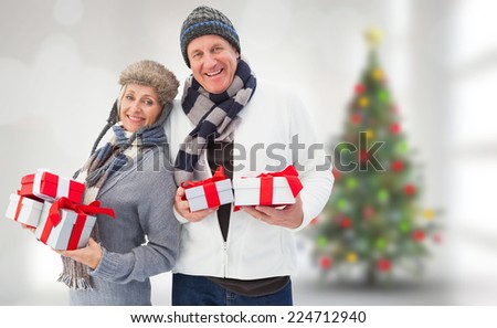 Festive mature couple holding christmas gifts against blurry christmas tree in room