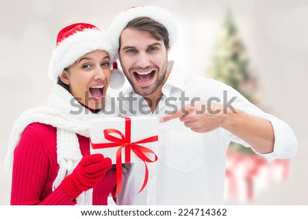 Festive young couple holding gift against blurry christmas tree in room