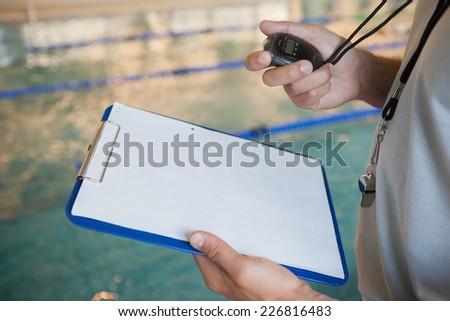 Swimming coach looking at his stopwatch by the pool at the leisure center