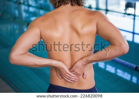 Close up mid section of a shirtless fit swimmer with back ache by the pool