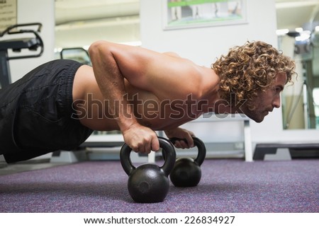 Side view of a handsome young man doing push ups with kettle bells in gym