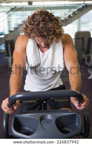 Determined handsome young man working out on exercise bike at the gym