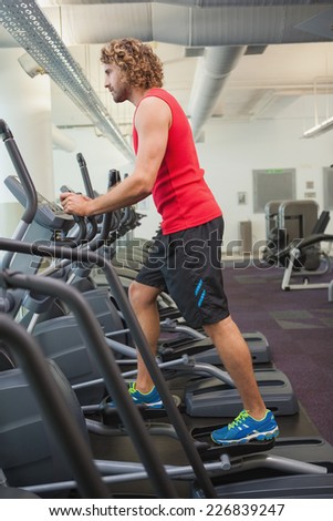 Side view of a young man working out on x-trainer in the gym