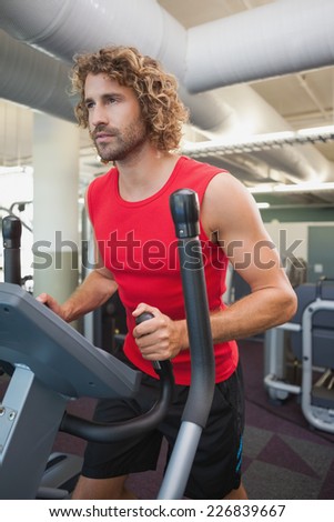 Determined young man working out on x-trainer in the gym