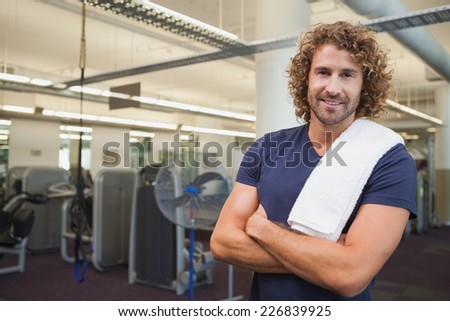Portrait of a smiling handsome trainer with arms crossed standing in the gym