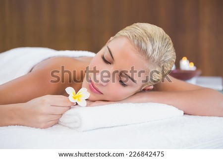 Close up of a beautiful young woman holding flower on massage table at spa center