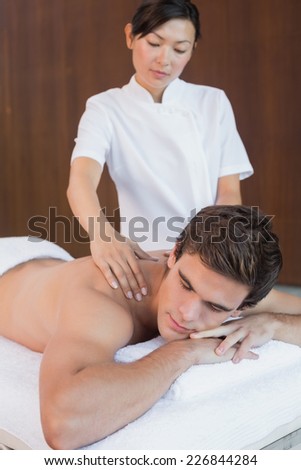 Close up of a handsome young man receiving shoulder massage at spa center