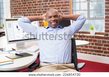 Portrait of young businessman sitting with hands behind head at office desk
