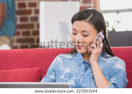 Young casual woman using laptop and mobile phone on couch in the office