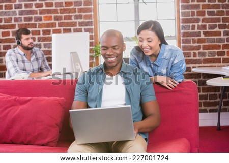 Young casual colleagues using laptop on couch in the office