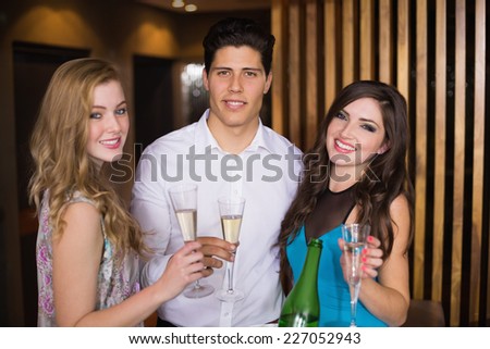 Attractive friends smiling at camera holding champagne at the bar