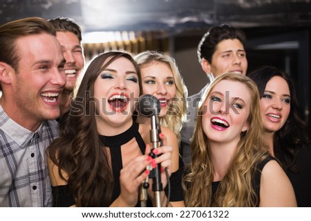 Happy friends singing karaoke together at the bar