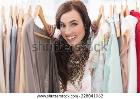 Pretty brunette smiling at camera by clothes rail at clothes store