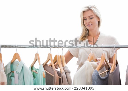 Pretty blonde looking through clothes rail on white background