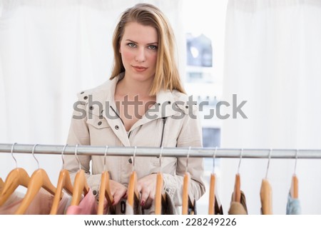 Pretty blonde looking at camera by clothes rail in the store