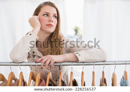 Pretty blonde thinking through clothes rail in the store