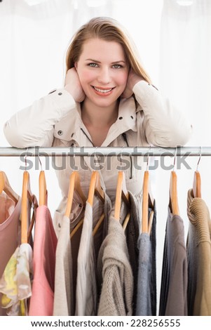 Pretty blonde smiling at camera by clothes rail in the store
