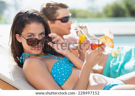Side view of a young couple with drinks by swimming pool