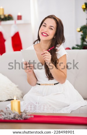 Brunette lying on the couch writing her christmas list at home in the living room