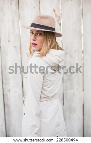 Pretty blonde woman with hat looking over her shoulder in front of a wooden wall