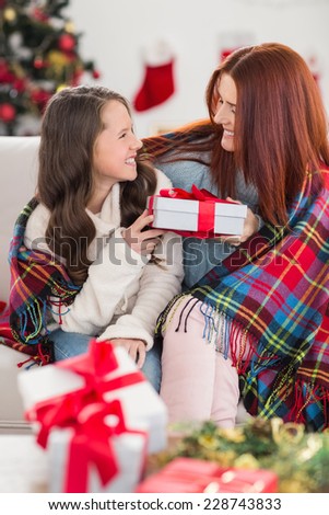 Festive mother and daughter wrapped in blanket with gifts at home in the living room