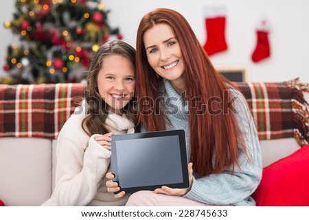 Festive mother and daughter showing tablet on the couch at home in the living room
