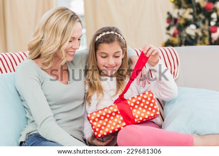 Cute little girl sitting on couch opening gift with mum at home in the living room