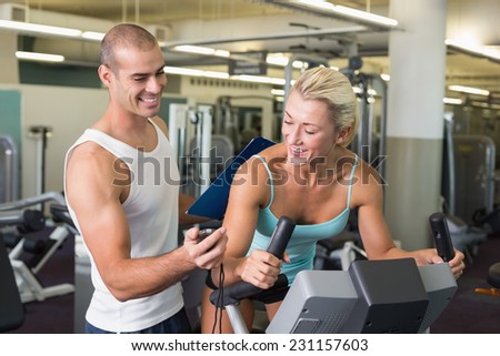 Smiling male trainer timing his client on exercise bike at the gym