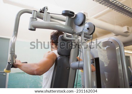 Fit man using weights machine for arms at the gym