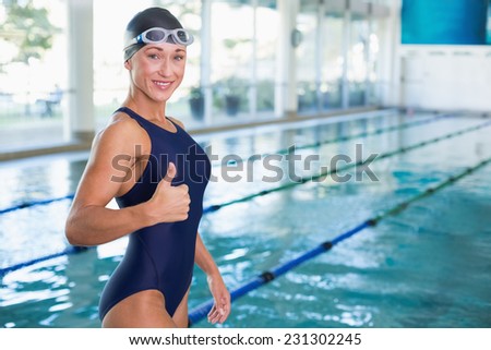 Portrait of a fit female swimmer gesturing thumbs up by the pool at leisure center